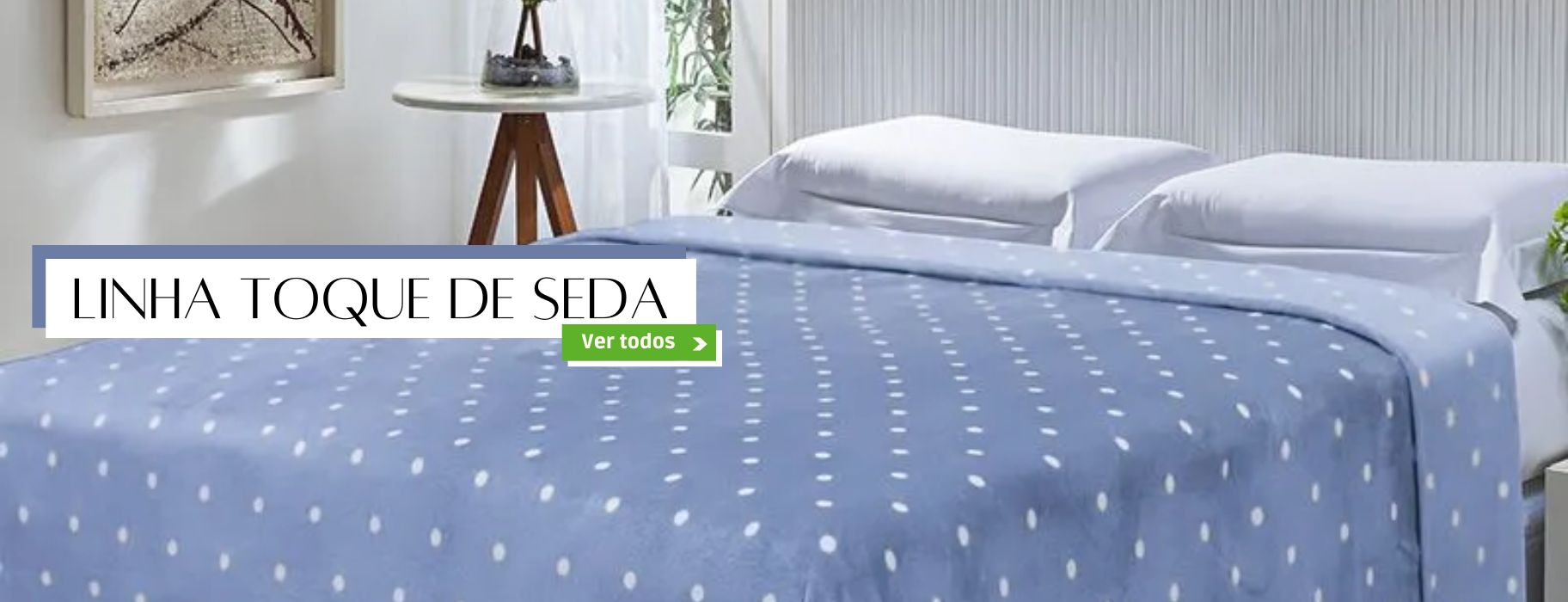 Banner promocional apresentando uma cama com roupa de cama azul clara de bolinhas brancas, destacando a "LINHA TOQUE DE SEDA". O botão "Ver todos" convida a explorar a coleção completa de produtos com toque suave e sedoso, como lençóis e fronhas.